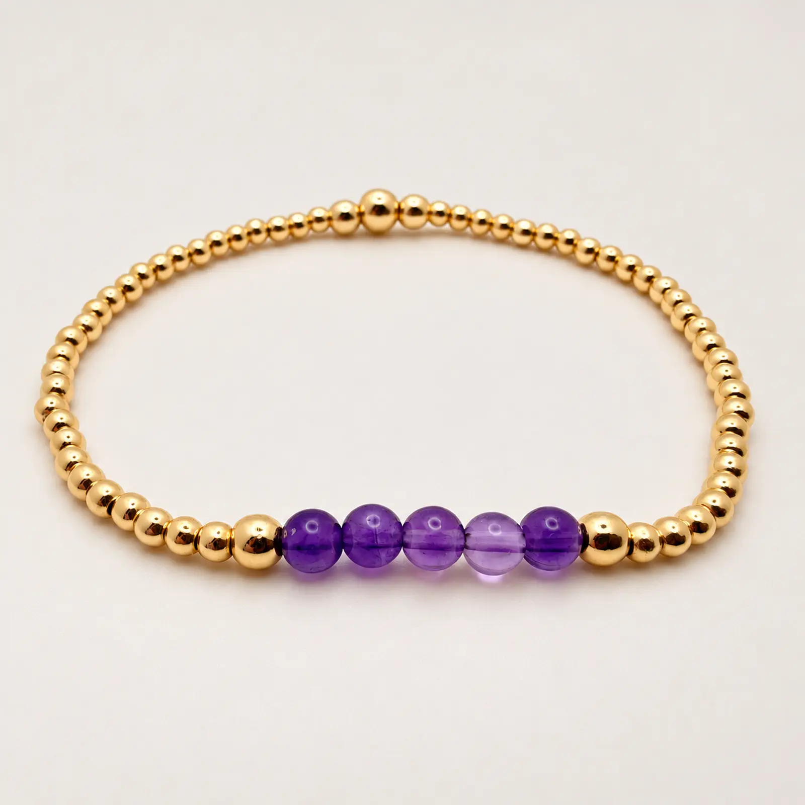 The Dianne stretch bracelet arranged in a circle, with five purple amethyst beads centered between polished 14K gold-filled beads
